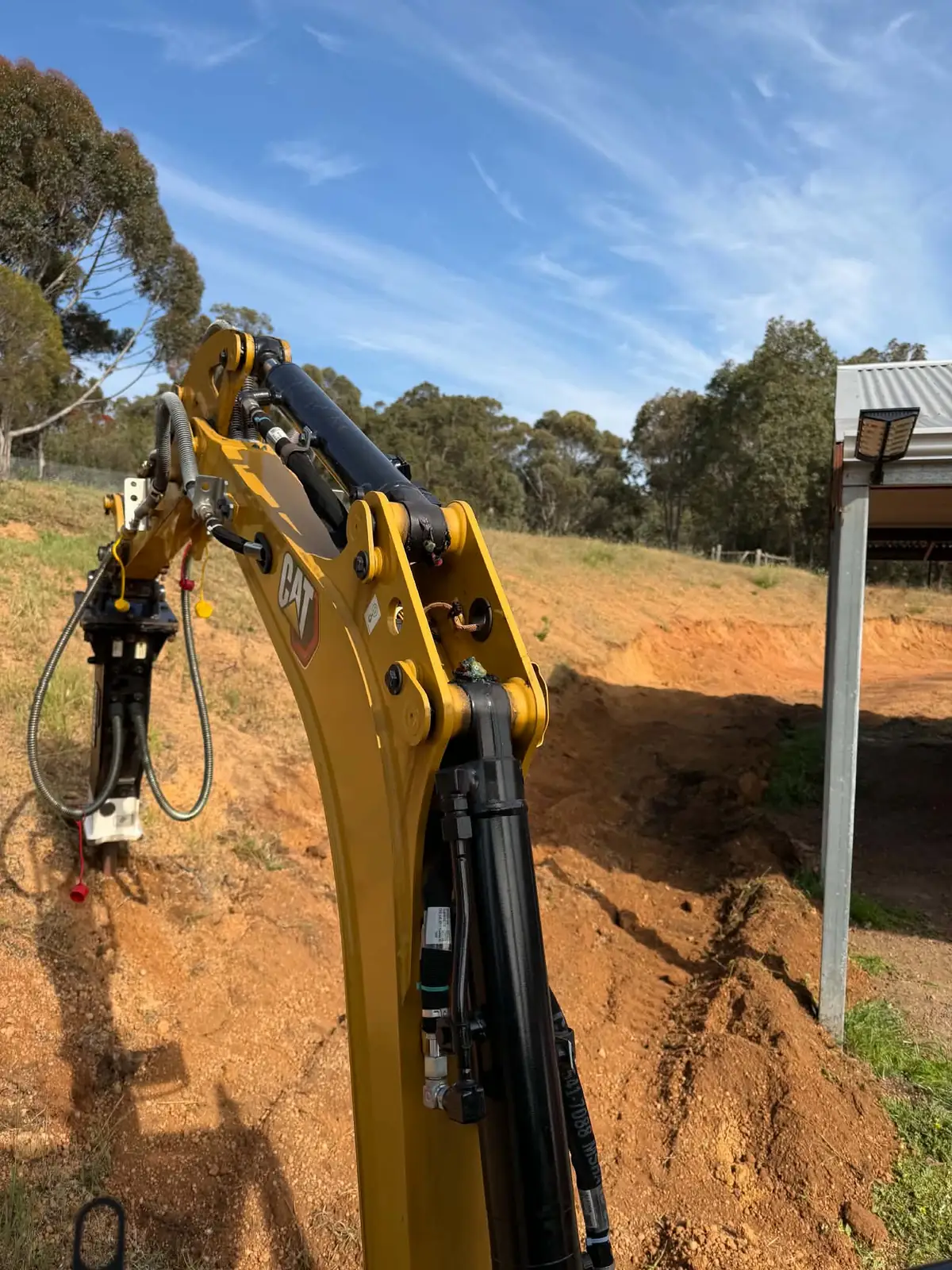 Close view of the Cat boom and arm with a hydraulic attachment fitted, against a red dirt slope and blue sky
