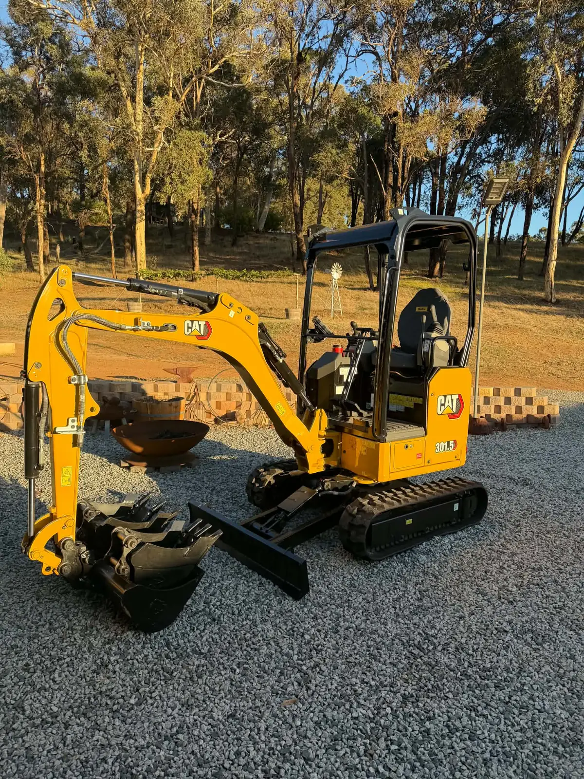Yellow Cat 301.5 mini excavator on a gravel pad at golden hour, with its bucket set and dozer blade visible