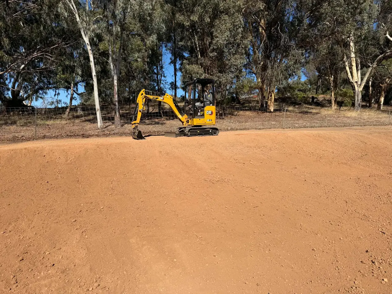 Yellow Cat 301.5 mini excavator working at the top of a freshly graded red dirt pad, with gum trees behind