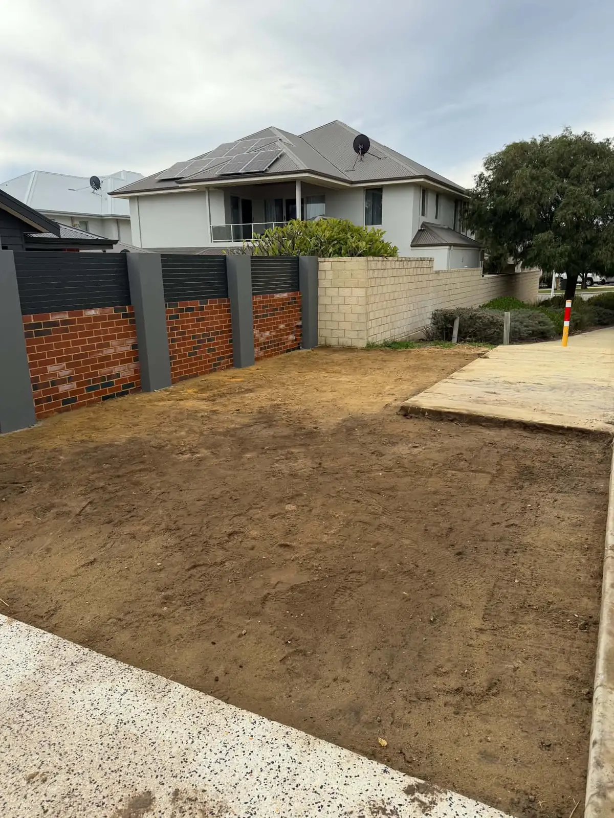 The same lot after earthworks: a level, trimmed sand pad in front of the brick and slat fence, ready for the next trade