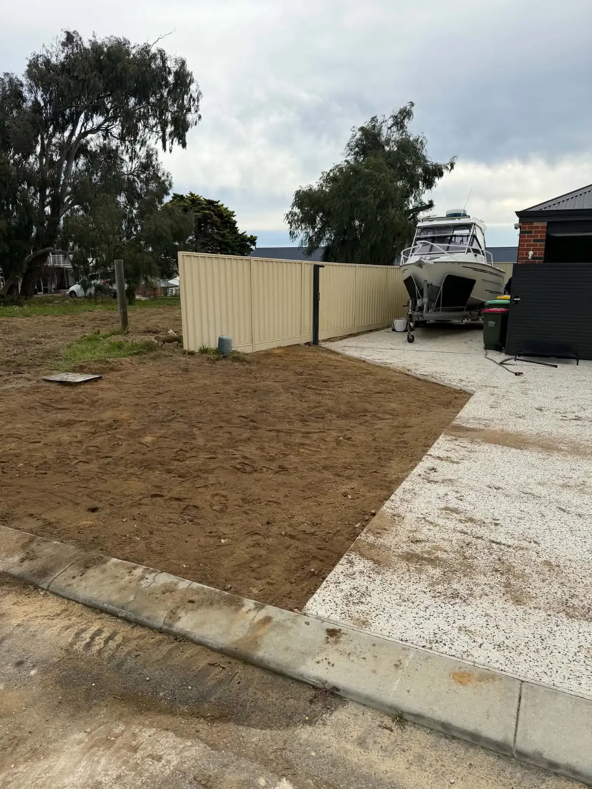 Levelled sand pad between a kerb and a new aggregate driveway, with a boat on a trailer beyond a Colorbond fence