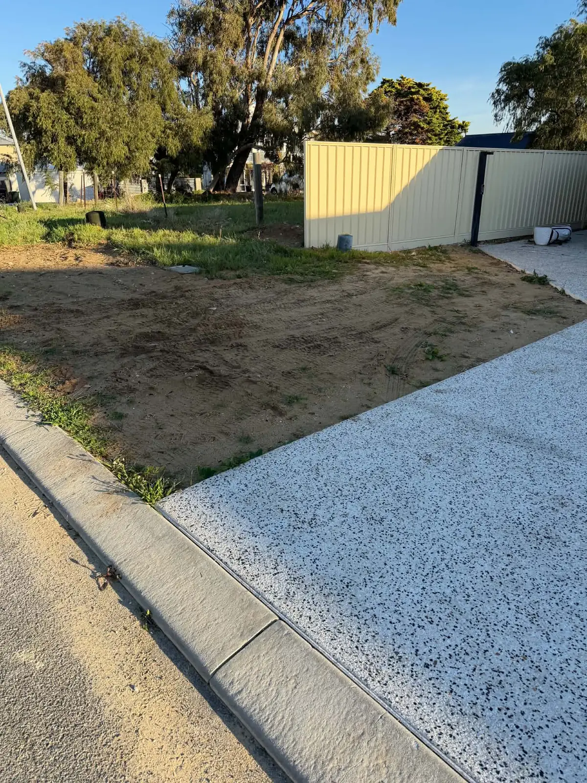 Scraped and trimmed sand verge beside a new exposed aggregate driveway and a Colorbond fence